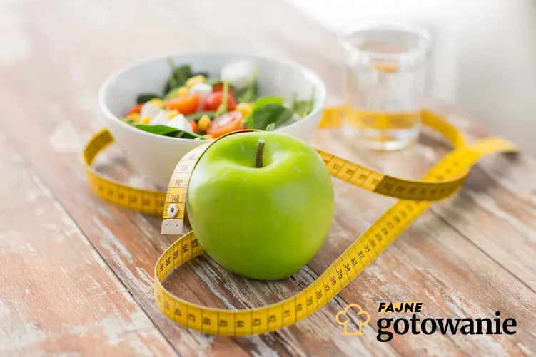 Na blacie leży zielone jabłko, miarka oraz miska z warzywami, efekty stosowania diety jabłkowej, czy dieta jabłkowa jest dobra na żołądek