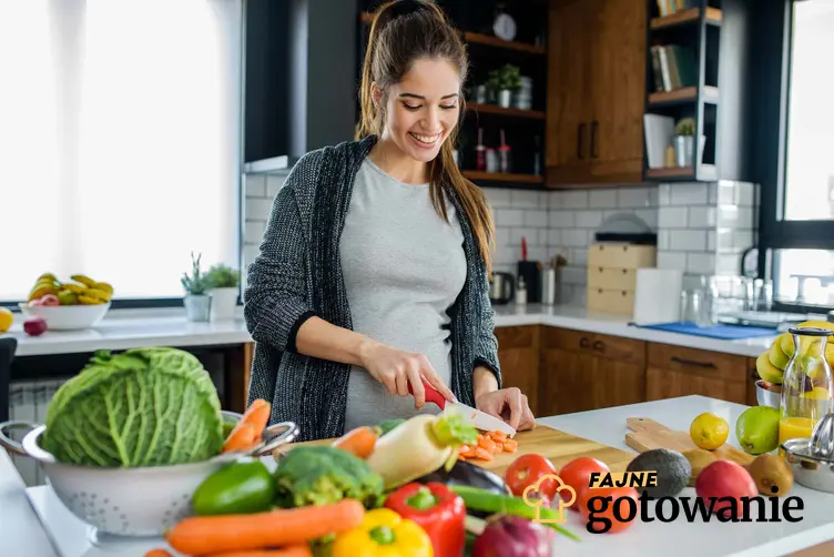 Młoda kobieta w kuchni przy blacie pełnym warzyw i owoców, warzywa i owoce na blacie w kuchni, ile posiłków dziennie spożywać w diecie warzywno-owocowej