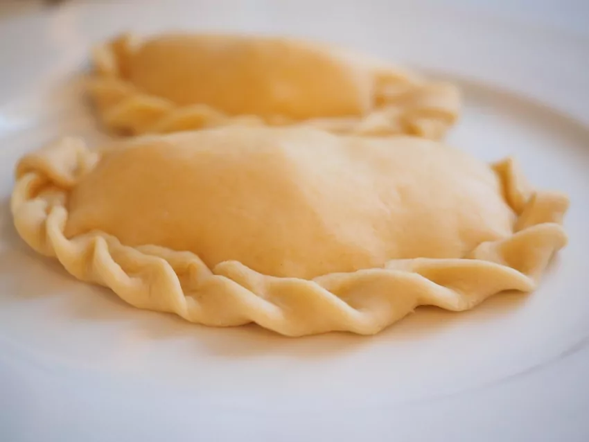 Pierogi gotuj w osolonej wodzie partiami, aby się nie sklejały Zbliżenie na 2 surowe pierogi, ozdobione charakterystycznym falowanym brzegiem