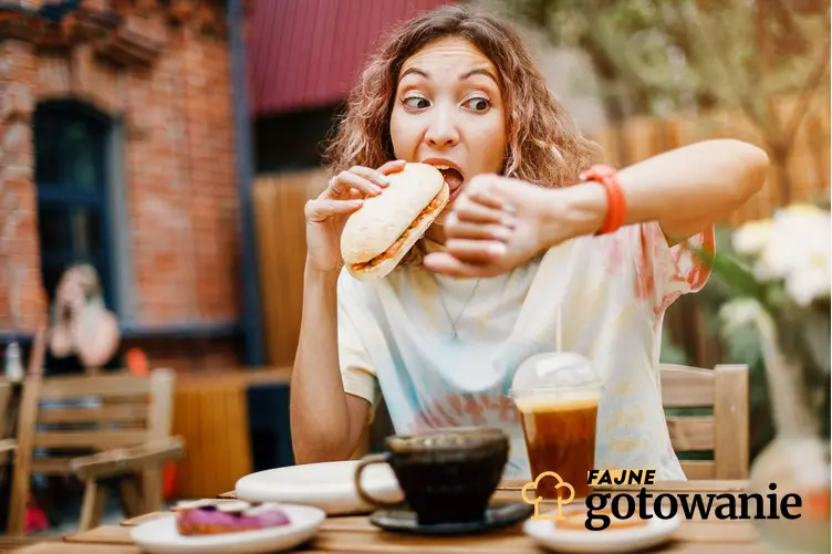 Kobieta gryzie kanapkę, spoglądając nerwowo na zegarek, na stole stoi też kawa i napój oraz inne przekąski., a także wpływ złych nawyków żywieniowych na zdrowie.