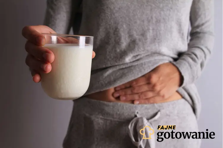 Kobieta trzyma się za brzuch jedną ręką, a w drugiej trzyma szklankę mleka, a także jakie są objawy nietolerancji laktozy