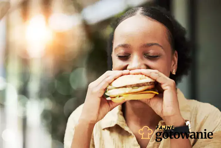 Kobieta z hamburgerem, uśmiechnięta.