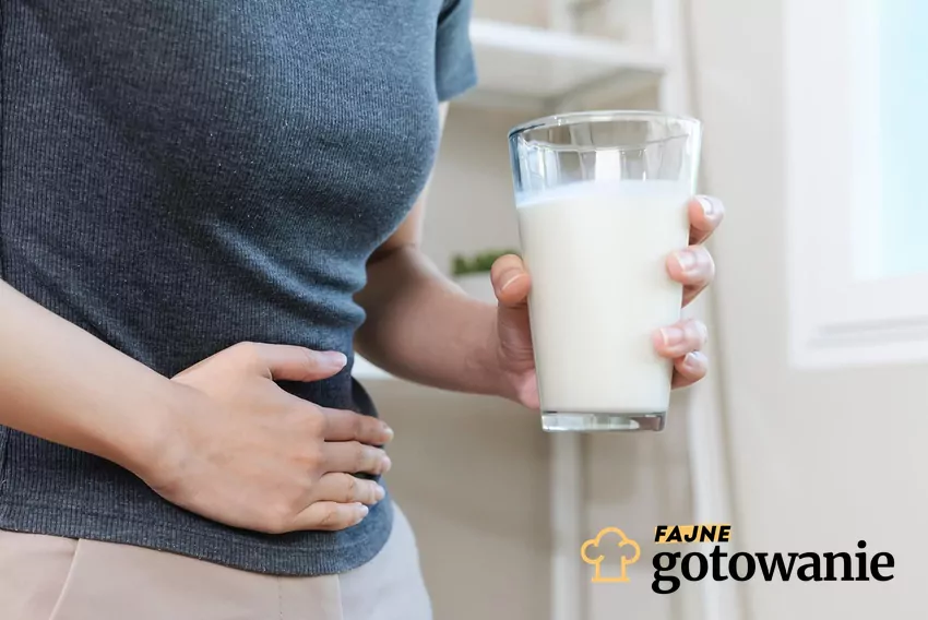 Biegunki i ból brzucha to najczęstsze objawy nietolerancji laktozy Kobueta trzyma szklankę mleka, a drugą ręką trzyma się za brzuch
