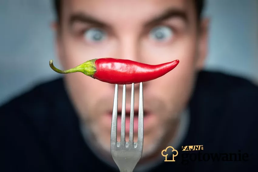 Mężczyzna trzyma w dłoni widelec, na którym jest papryczka chilli