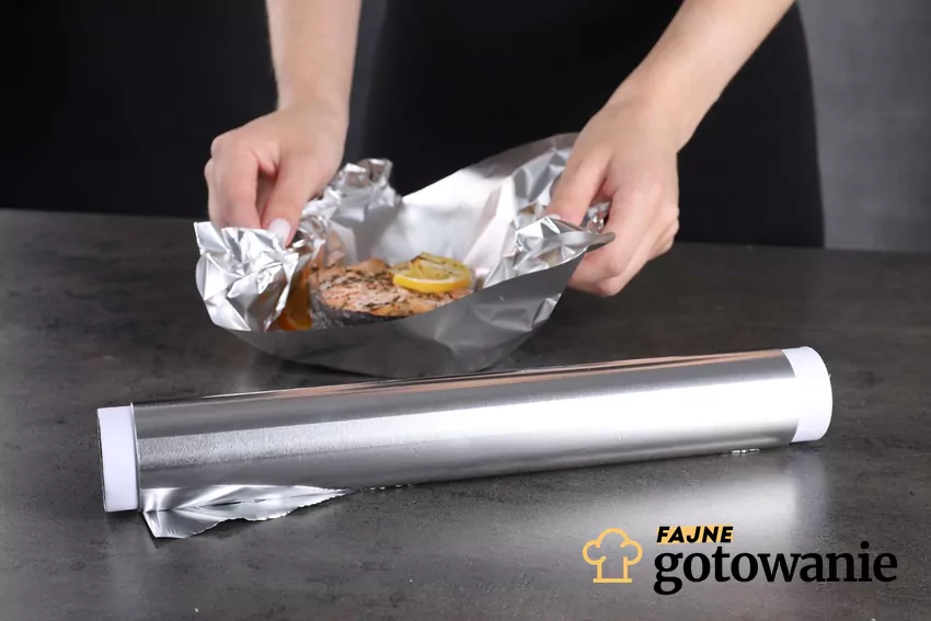 Folia aluminiowa bezpieczna tylko w niskich temperaturach – nie używaj jej w piekarniku ani na grillu Kobieta owija rybę w folię