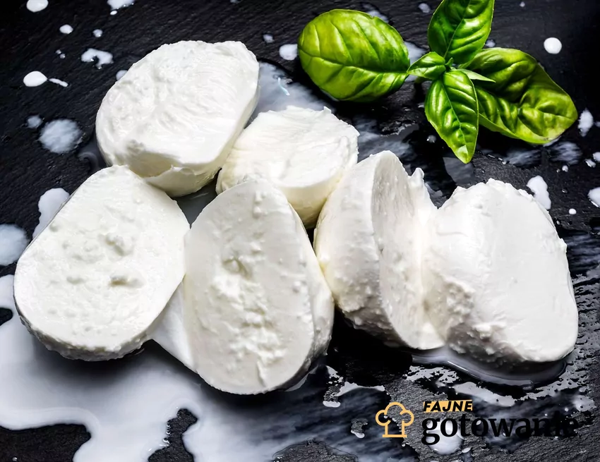 Plastry mozzarelli na czarnej desce z liśćmi bazylii