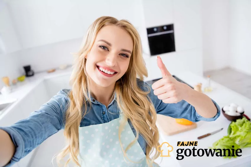 Kobieta robi sobie selfie w kuchni w fartuszku i wyciąga przed siebie uniesiony kciuk w górę, opinie lekarzy na temat diety selfie, jak przestrzegać diety selfie, dieta selfie a motywacja