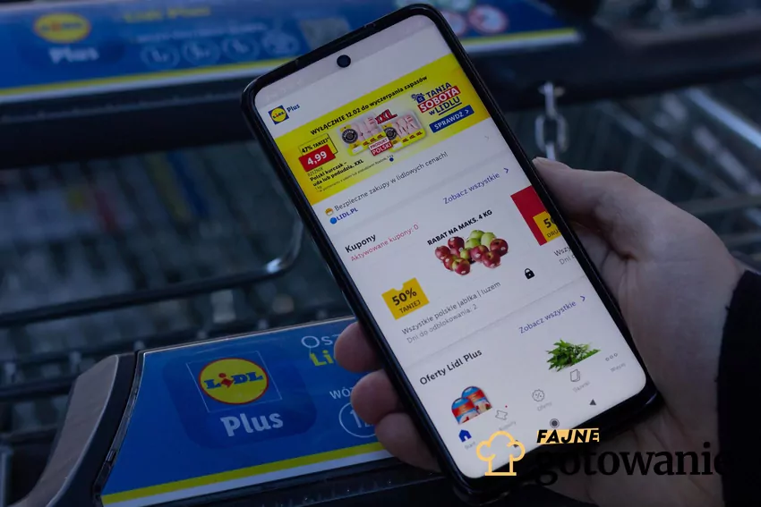Aplikacja Lidl Plus w telefonie na tle wózka sklepowego