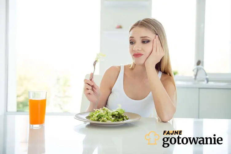 Kobieta siedzi przy stole i je sałatkę, na twarzy ma grymas, a także dlaczego oliwa w za dużej ilości jest gorzka