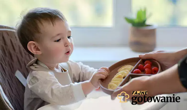 Dziecko sięgające po talerzyk z owocami