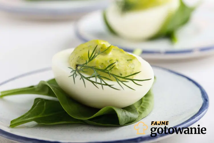 Jajko faszerowane awokado podane na białym talerzyku. Jajko ułozona jest na liściach szpinaku.