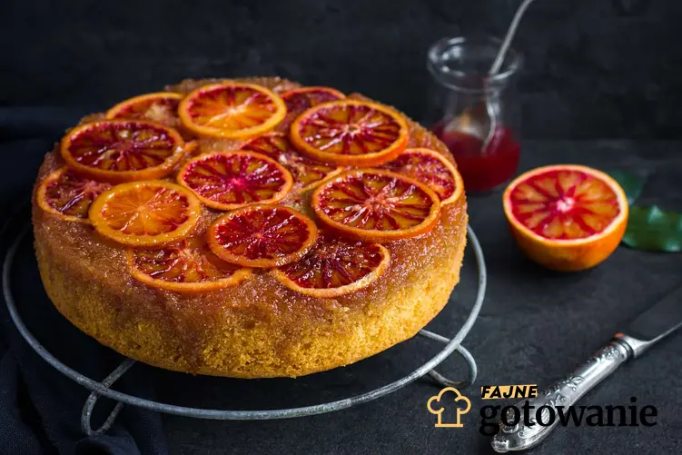 Sycylijskie ciasto pomarańczowe z plasterkami pomarańczy na wierzchu na tle pomarańczy sycylijskich.