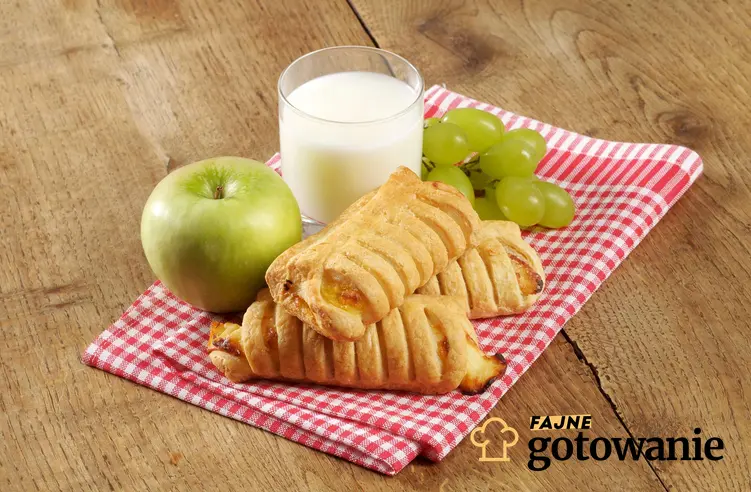Bułeczki z ciasta francuskiego podane na serwecie kuchennej wraz z mlekiem i jabłkiem.