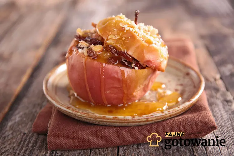 Pieczone jabłka z miodem podane na talerzyku posypane posiekanymi, prażonymi migdałami.