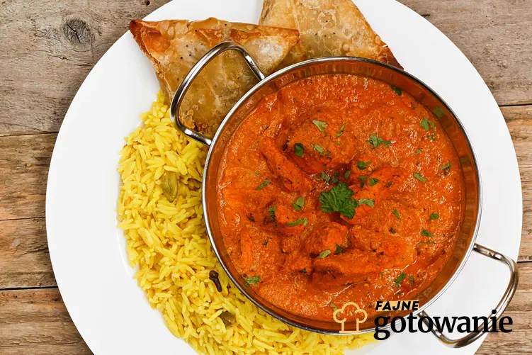 Czerwone curry podane z dodatkiem ryżu. Całość znajduje się na białym talerzu.