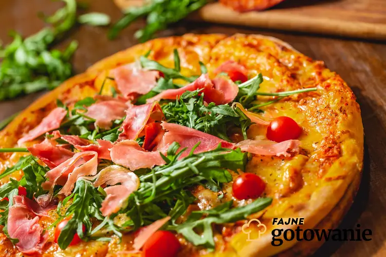 Pizza z szynką parmeńską ułożona jest na drewnianej, okrągłej desce.