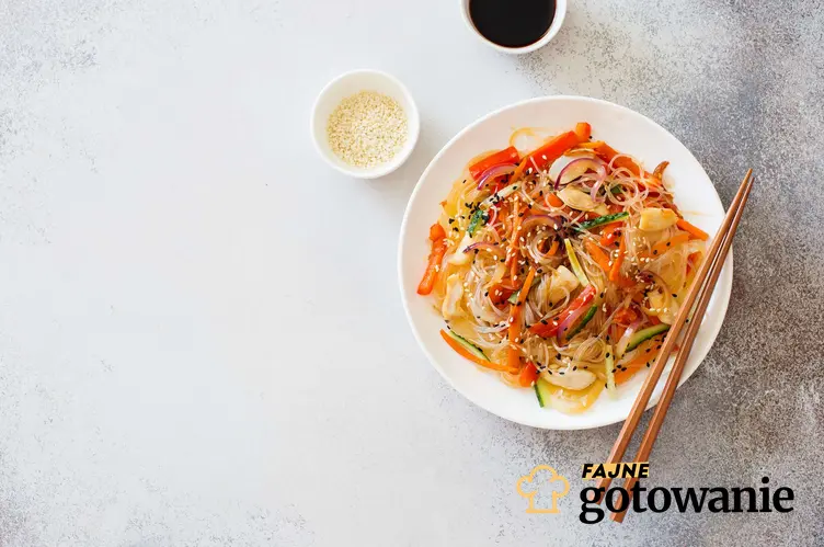 Sałatka z makaronem ryżowym i świeżymi warzywami w stylu orientalnym. Podana na okrągłym talerzyku z pałeczkami i sosem sojowym.
