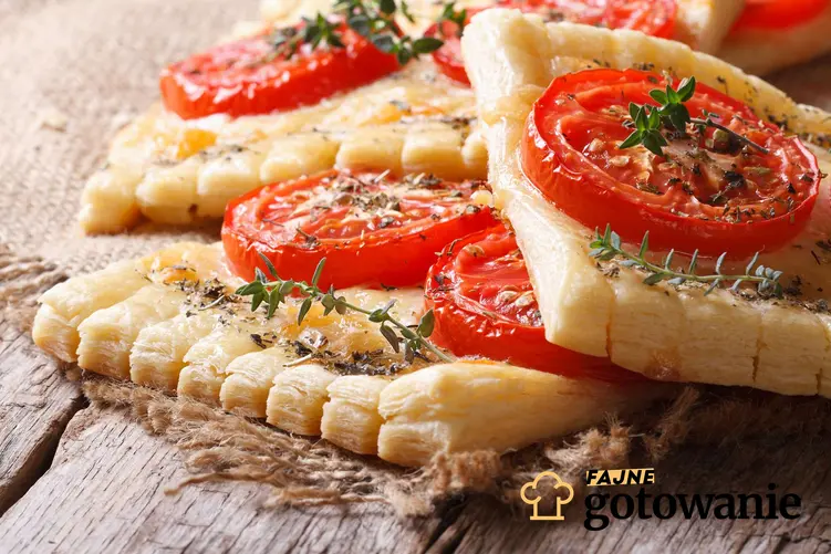 Ciasto francuskie z pomidorami podane na materiale, który lezy na drewnianym blacie.