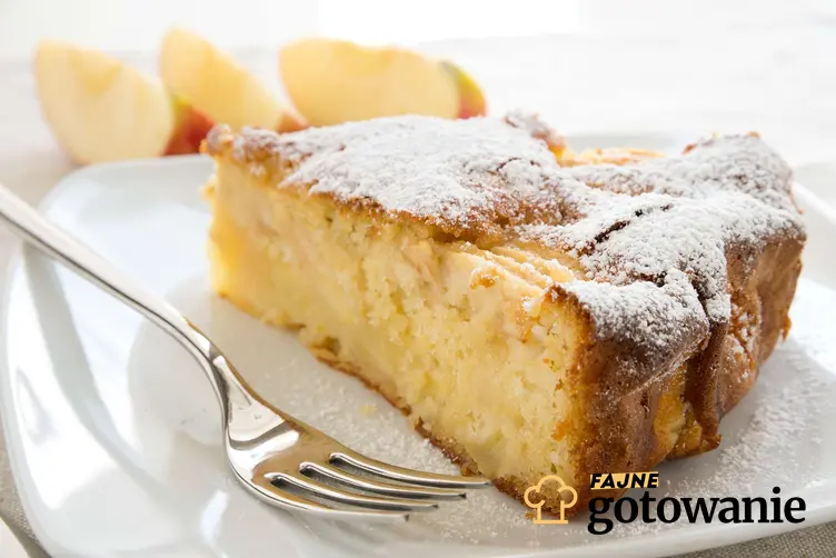 Kawałek ciasta z jabłkami, podany na talerzyku deserowym i posypany cukrem pudrem.