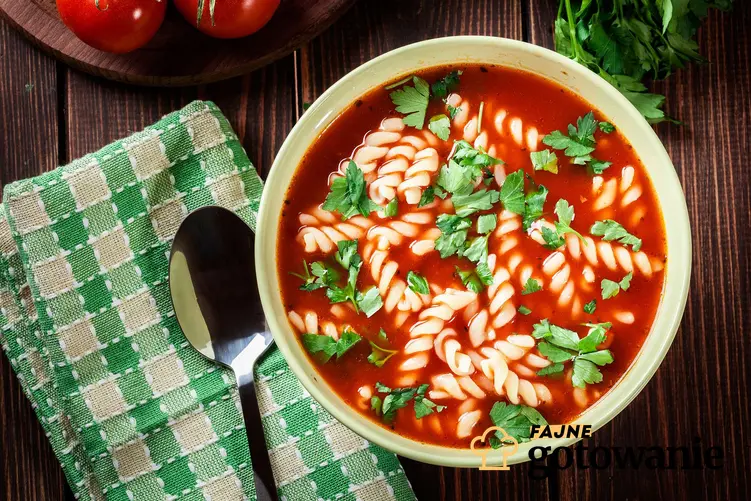 Zupa pomidorowa z makaronem umieszczona w dekoracyjnym głębokim talerzu, posypana natką pietruszki.