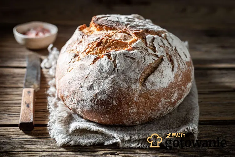 Chleb na proszku do pieczenia podany na ściereczce leżącej na drewnianym blacie. Obok chleba leży nóż.