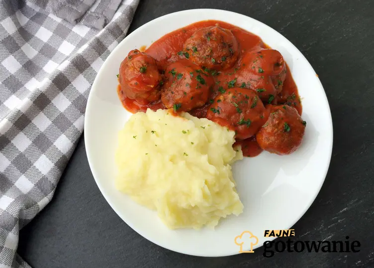 Pulpety w sosie pomidorowym z ziemniakami podane na białym talerzu.