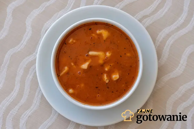 Zupa pomidorowa z lanymi kluskami podana w białej miseczce.