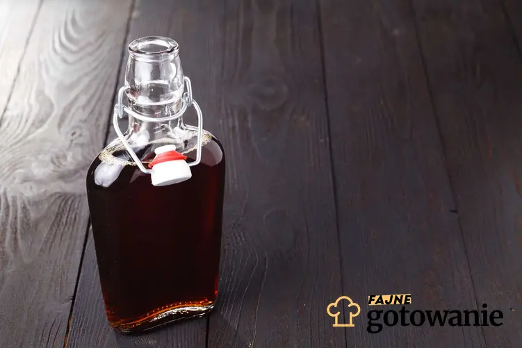 Nalewka malinowa na spirytusie podane w szklanej butelce, która stoi na ciemnym, drewnianym blacie.