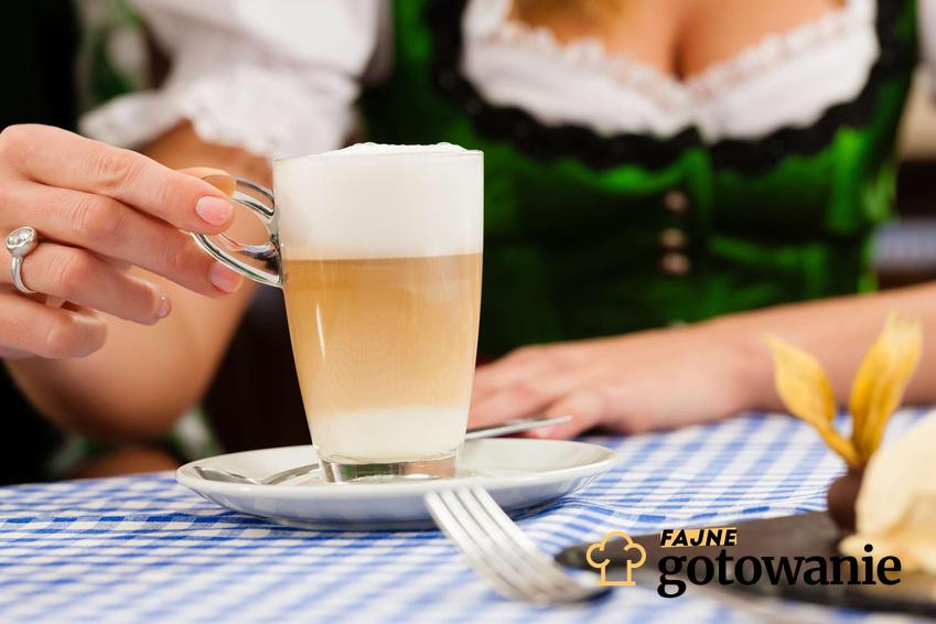 Kawa po bawarsku podana w szklance, która stoi na białym talerzyku.