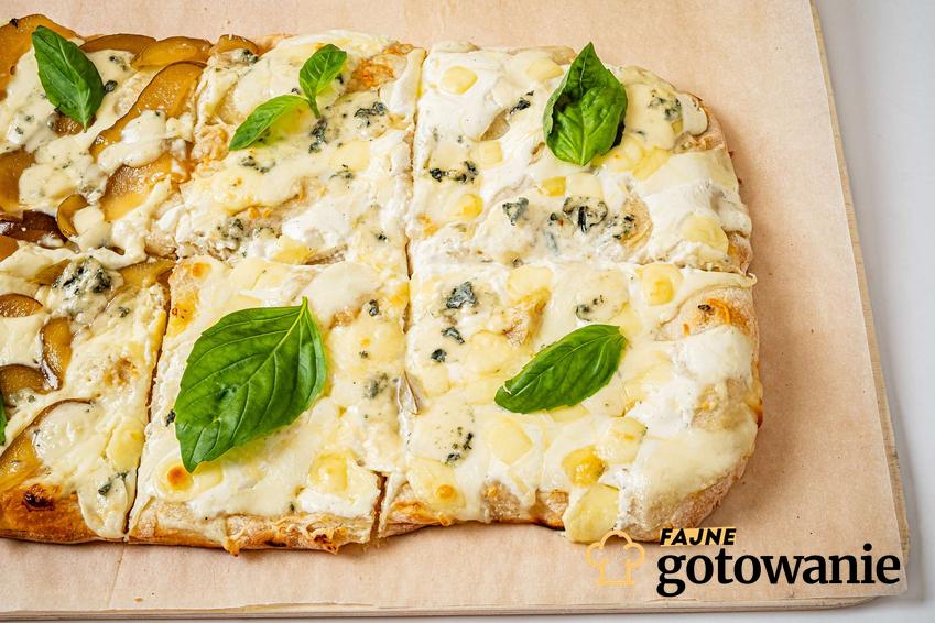 Pizza z serem pleśniowym ułożona na desce pokrytej papierem do pieczenia.