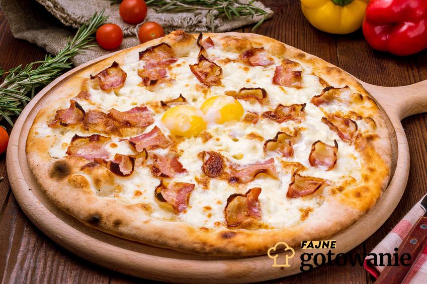 Pizza carbonara podana na drewnianej desce.