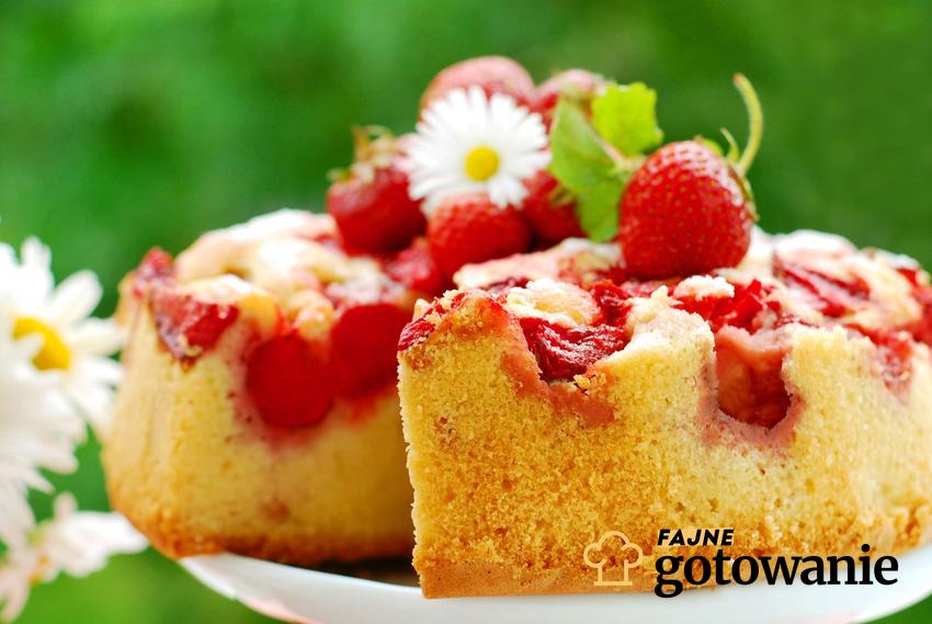 Ciasto biszkoptowe z truskawkami udekorowane świeżymi owocami, kwiatami i listkami mięsny.
