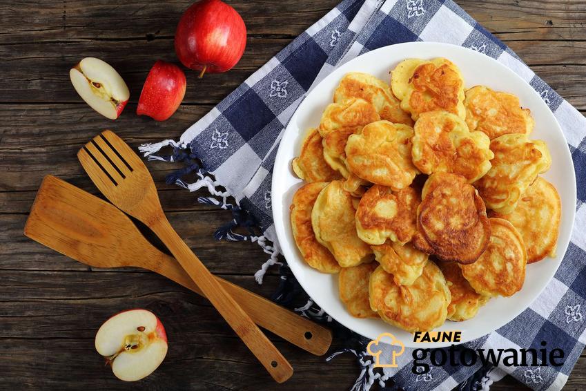 Racuchy na kefirze podane na dużym talerzu z jabłkami w tle.