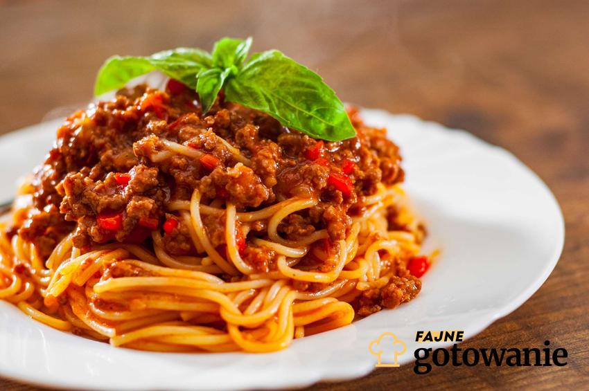 Włoskie spaghetti w sosie mięsno pomidorowym udekorowane listkiem świeżej bazylii