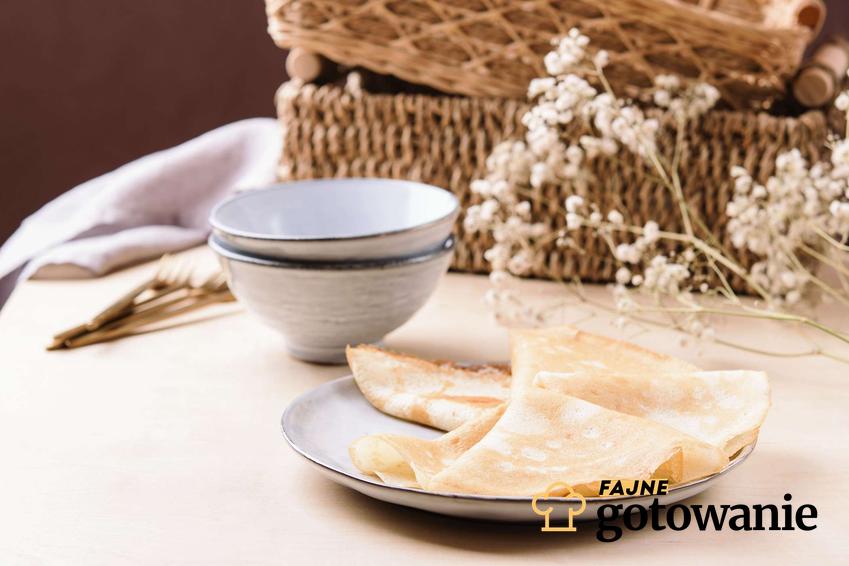 Naleśniki z mąki ryżowej podane na szarym talerzu, w tle szare miseczki, białe gałązki i wiklinowy kosz