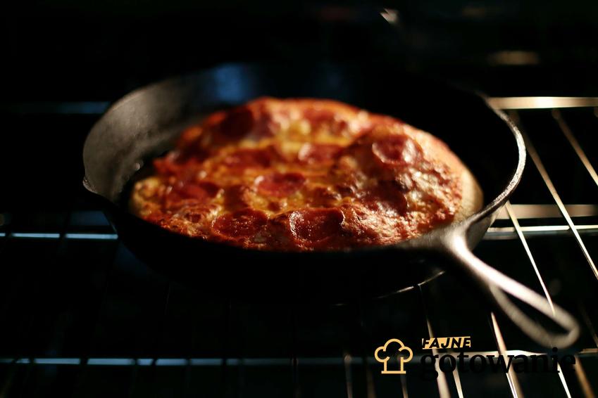 Upieczona fit pizza z patelni z dodatkiem salami znajduje się w patelni na kuchence.