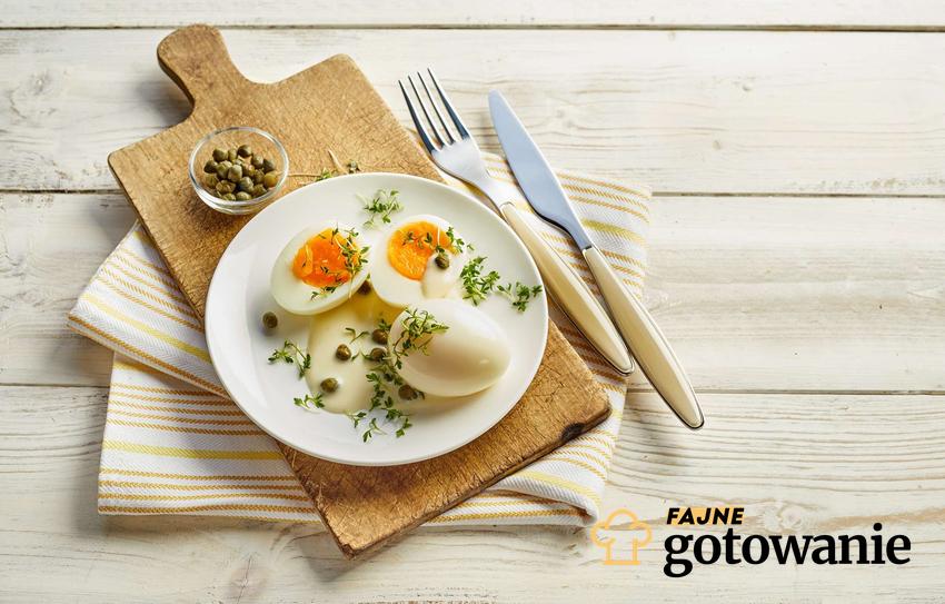 Jajka w sosie musztardowym podane na białym talerzu, który stoi na drewnianej desce.