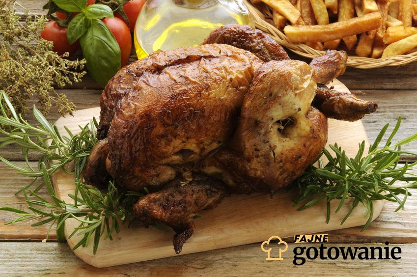 Kurczak pieczony w całości, z gałązkami świeżego rozmaryny, na drewnianej desce do krojenia.
