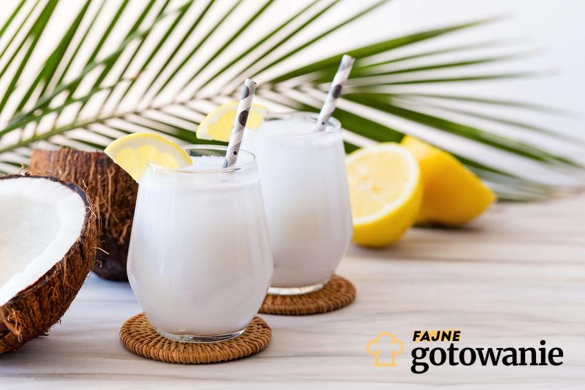 Drink kokosowy podany w ozdobnych szklankach. W każdej szklance znajduje się słomka. Na stole oprócz szklanek znajdują się połówki kokosa oraz cytryny.