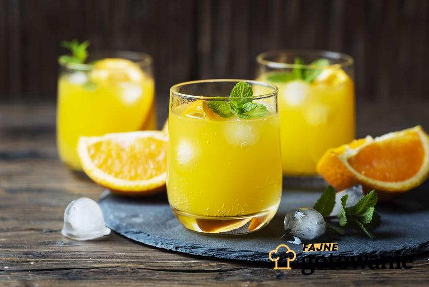 Drink z sokiem pomarańczowym podany w szklance. Obok niego znajdują się kawałki pomarańczy.