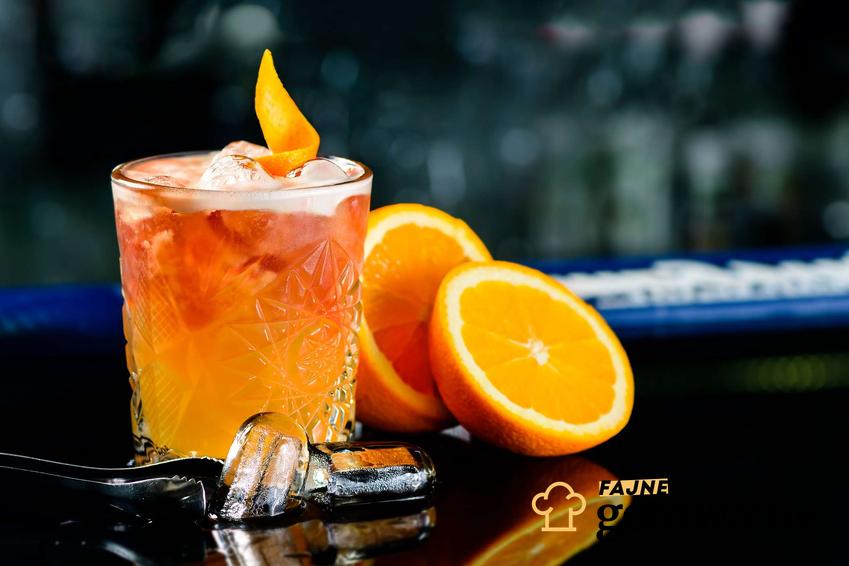 Drink z amaretto podany jest w szklance. Obok niej znajdują się kawałki pomarańczy oraz kostki lodu.