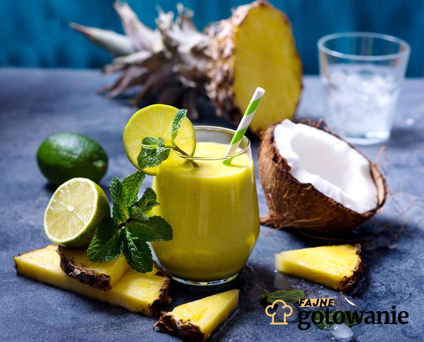 Koktajl z ananasa podany w szklance. Dookoła niej ułożony jest ananasa, kokos oraz listki mięty.