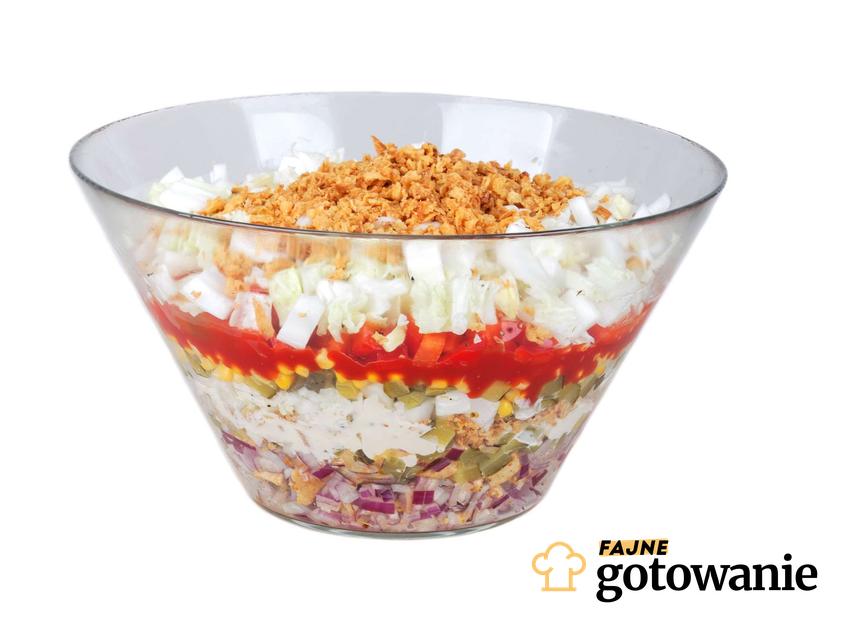 Sałatka gyros znajduje się w szklanej, przezroczystej salaterce.Widzimy poukładane warstwami produkty sałatki.