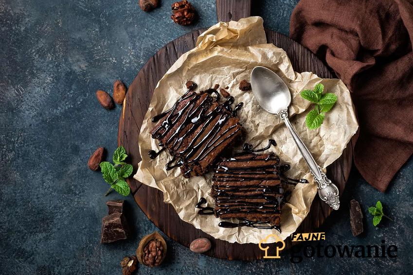 Wegańskie ciasto czekoladowe podane na drewnianej desce z czekoladą i kakao.