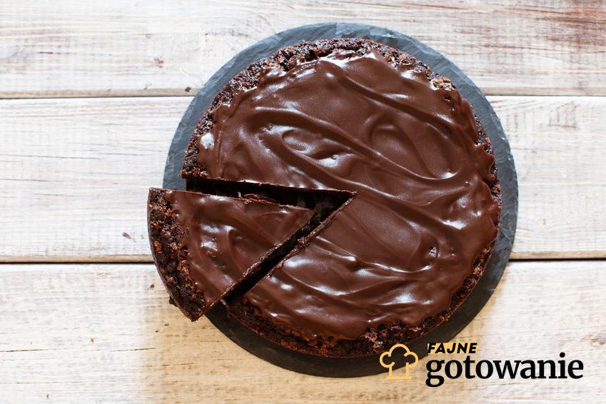 Ciasto czekoladowe z kremem podane na paterze stojącej na drewnianym blacie.