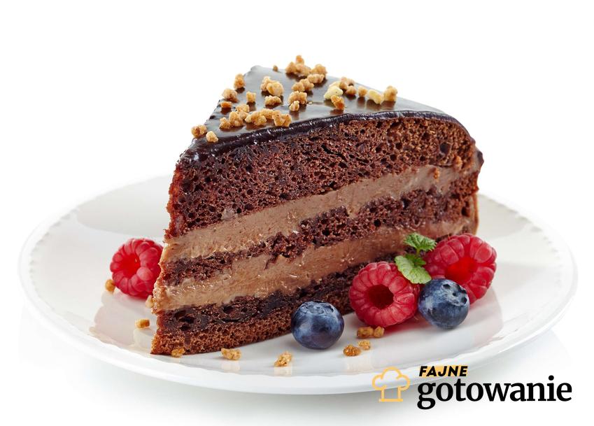 Szybkie ciasto czekoladowe z kremem ozdobione malinami i borówkami podane na białym talerzyku.