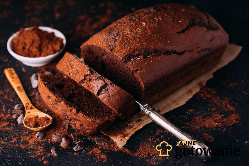 Wilgotne ciasto kakaowe pokrojone na kawałki podane na papierze do pieczenia. Dookoła ciasta rozsypane jest kakao.