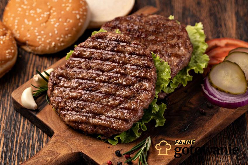 Mięso na hamburgery podane na desce z warzywami.
