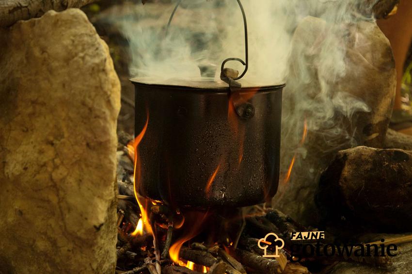 Kociołek na ognisko znajduje się nad ogniskiem. W kociołku przygotowywana jest pyszna potrawa.
