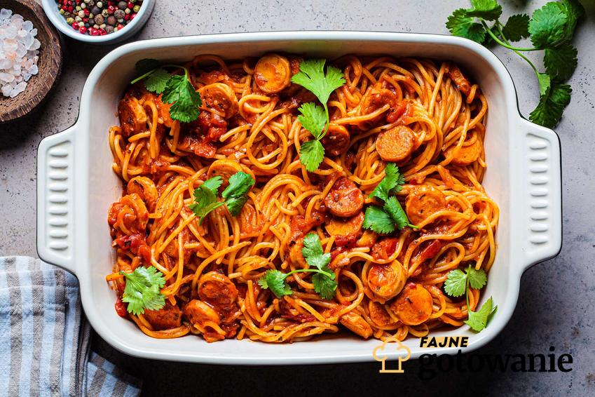 Spaghetti z kiełbasą udekorowane bazylią.